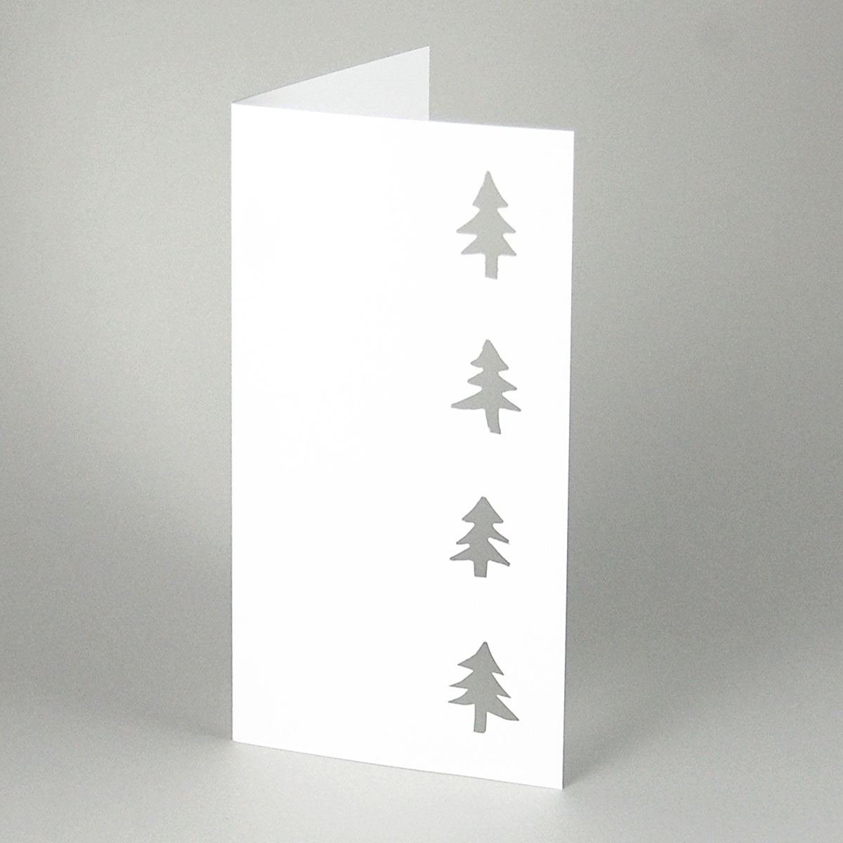weiße Weihnachtskarte mit ausgestanzten Tannenbäumen